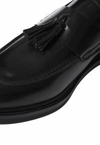 Mocassino in pelle nera con finitura liscia, caratterizzato da un dettaglio decorativo a nappine e cuciture lungo il bordo della suola.