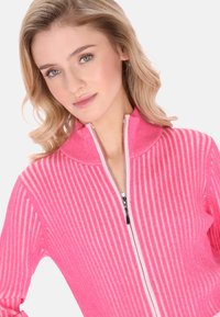 Eng anliegende rosa Reißverschlussjacke mit geripptem Muster, ausgestattet mit hohem Kragen und kontrastierendem Reißverschluss. Der Stoff hat einen dezenten Glanz und vertikale Streifen.