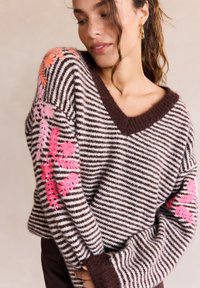 Maglione a righe marrone e crema con scollatura profonda a V. Presenta ricami floreali in rosa e corallo sulle maniche e polsini a coste. Tessuto morbido.