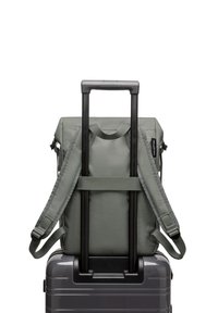 Sac à dos en tissu vert avec des bretelles ajustables, attaché à une valise grise. Le sac à dos dispose d'une poignée supérieure et d'une texture lisse.