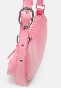 Borsa a tracolla in pelle sintetica rosa con forma piatta, hardware in argento e una larga tracolla con accenti circolari. Chiusura aZIP nella parte superiore.
