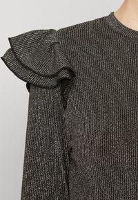 Top in maglia a coste nera con filo lucido, scollo rotondo e accentuazioni arricciate sulle spalle. Tessuto testurizzato con linee verticali.