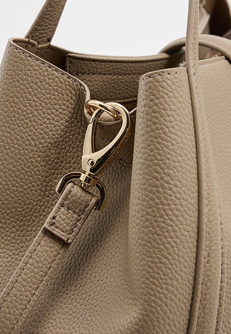 Beige lederen handtas met een geribbelde textuur, voorzien van een gouden metalen sluiting en stikdetails op de band.
