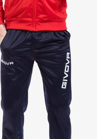 Giacca a track rossa abbinata a pantaloni sportivi blu navy con una texture lucida e il logo bianco "GIVOVA" sul lato.