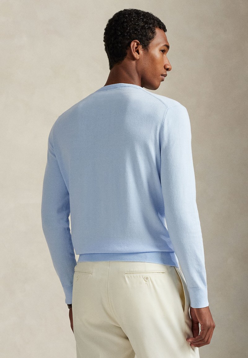 Maglione azzurro chiaro lavorato a maglia con maniche lunghe e scollo rotondo, caratterizzato da una vestibilità aderente e bordi a costine su polsini e orlo. Indossato con pantaloni di colore chiaro.