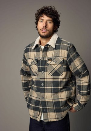 Flannel shirt with a black and beige plaid pattern, featuring a soft cream-colored collar, two chest pockets, and button closures.