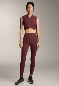 Completo sportivo color bordeaux composto da un top corto senza maniche con design twist e leggings a vita alta, entrambi realizzati in un tessuto liscio ed elastico.