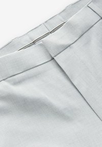 Hellgrauer Stoff mit glatter Textur. Verfügt über einen flachen Bund und eine einzelne Kellerfalte als Designdetail. Sichtweise eines Rocks oder einer Hose.