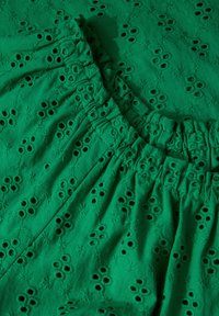 Tessuto verde con motivi floreali ricamati e dettagli in occhielli. Presenta un colletto arricciato ed elasticizzato e una superficie strutturata.