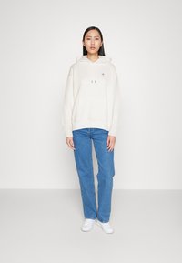Witte hoodie met trekkoord, voorzak, gecombineerd met blauwe rechte jeans en witte sneakers. Eenvoudige, gladde textuur, minimale branding.