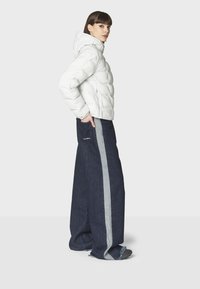 Hvid pufferjakke med hætte, parret med bredbenede mørk denim bukser med grå side striber og frynset kant.