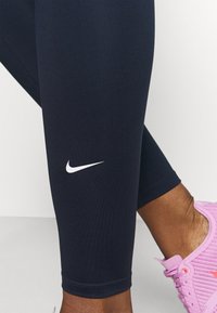 Leggings deportivos azul marino con un diseño ajustado, tejido suave y un logo blanco de Nike en la parte inferior de la pierna.