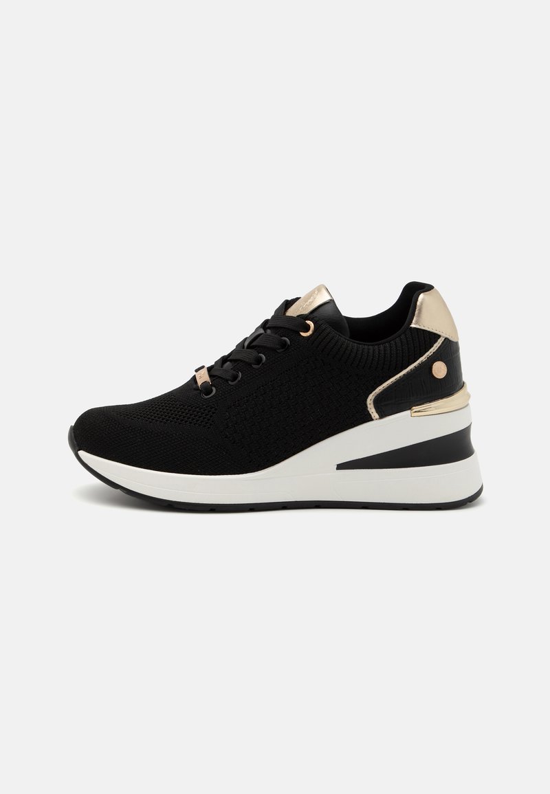 Black knit sneakers with a textured upper, gold accents, and a wedge sole featuring a white and black design. Laces and metal eyelets included.