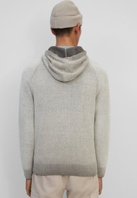Sudadera de punto gris claro con un cuello interior de un gris más oscuro, que presenta una capucha con cordón y puños acanalados. Textura suave, diseño casual.