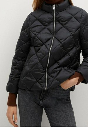 Sort quiltet jakke med diagonale syninger, sølv lynlås foran, båret over en brun langærmet sweater og kombineret med mørkegrå jeans.