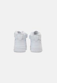 Zapatillas altas blancas con cuero liso, cuello acolchado, correas ajustables y suela de goma texturizada. La vista trasera muestra un diseño limpio.