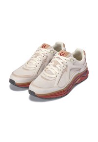 Zapatos deportivos beige con parte superior de malla, superposiciones texturizadas y una suela acolchada en rojo y marrón. Presenta cordones blancos y acentos de logo.