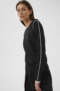 Mustast pehmest kangast pikkade varrukatega särk, millel on õmbluste ääres ja varrukaotsades kreemivärvi triibud ning lõdva istuvusega.