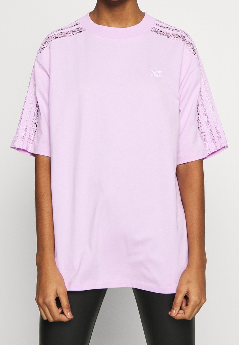 Rosa oversized t-shirt i bomull med spetsdetaljer längs axlarna och logotyptryck på bröstet. Korta ärmar, lös passform.