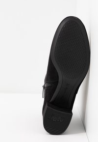 Černé nubukové kotníkové boty s texturovanou gumovou podešví. Mají boční zip a tvarovaný design, velikostní štítek viditelný na podešvi.