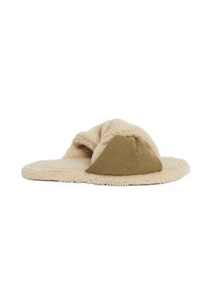 Beige fuzzy hjemmesko med en blød tekstur, der har et grønt lærredselement. Flad såledesign med en rund form.