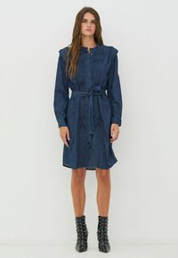 Gombos, hosszú ujjú farmer ruha, ráncolt részletekkel. Övvel a deréknál, bővülő alsó résszel és sötétkék színben.