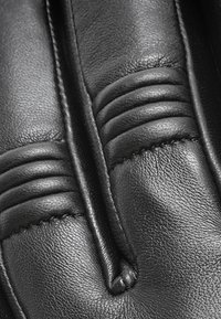 Svart läderhandske med sydda detaljer, med ribbade sektioner och en slät yta, som framhäver en intrikat hantverksskicklighet.