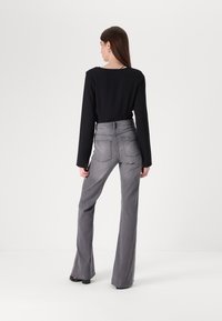 Juodas ilgomis rankovėmis džemperis, derinamas su aukšto juosmens, platėjančiomis pilkomis džinsais. Su siuvinėjimo detalėmis ir užpakalinėmis kišenėmis. Lygus audinio tekstūra.