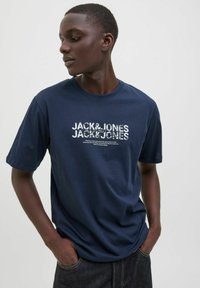 Marineblå bomulds t-shirt med et hvidt grafisk tryk af "JACK & JONES" på brystet, med korte ærmer og rund halsudskæring.