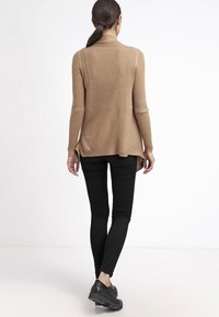 Haut à manches longues côtelé beige à ourlet asymétrique, associé à un jean skinny noir et des chaussures noires chunky, vu de dos.