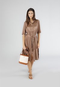 Brun, knäppt klänning med korta ärmar och knytning i midjan, i kombination med en kräm- och brun färgad bucket-väska och platta sandaler.