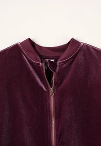 Burgundská sametová bomber bunda se zipem vpředu, žebrovaným límcem a měkkou texturou. Disponuje minimalistickým designem bez vzorů.