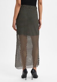 Schwarzer und goldener Netzrock mit einem Zickzackmuster, knielang, halbtransparentes Design, kombiniert mit schwarzen High Heels.