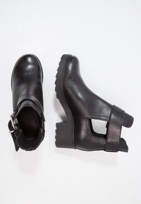 Czarne skórzane botki za kostkę z grubym obcasem, otwartym wzorem cięcia i bocznym paskiem z klamrą. Teksturowana czarna podeszwa dla lepszej przyczepności.