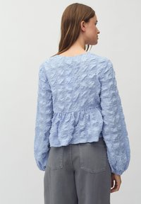 Svetlo modra bluzica z dolgo rokavi in peplum robom, ki ima občutljivo, gubano tkanino in okroglo ovratnik.