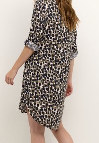 Robe chemise en tissu léger avec un motif abstrait multicolore. Comprend des manches retroussées et une fente sur le côté pour une meilleure aisance de mouvement.