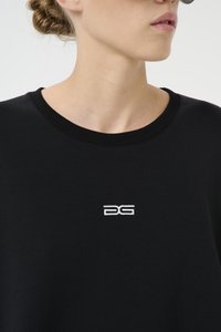 Svart sweatshirt med ribbet hals, med en liten hvit logo på brystet. Stoffet ser glatt ut med en myk tekstur.