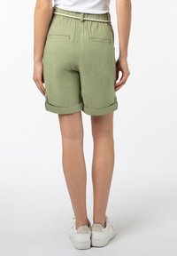 Green linen shorts with a soft texture, rolled cuffs, and an elastic waistband, featuring two back pockets and white sneakers.