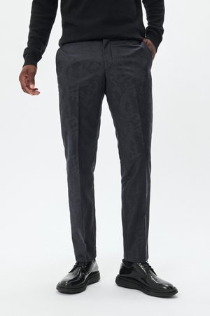 Pantalones de un gris oscuro con un patrón sutil, corte ajustado y bolsillos laterales, combinados con zapatos de charol negros.