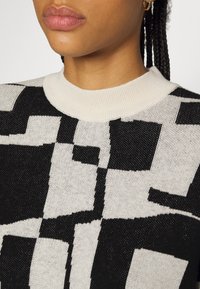 Gebreide trui met een zwart-wit geometrisch patroon, een ronde, roomkleurige geribbelde halslijn en een gestructureerde stof.