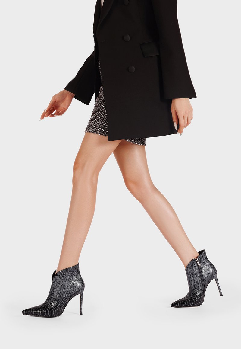 Stivaletti alla caviglia con stampa di serpente nera, punta affusolata, alti tacchi a stiletto e cerniere laterali, caratterizzati da una texture elegante e liscia.