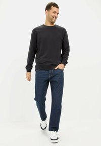 Schwarzer Sweatshirt mit Rundhalsausschnitt, gerippten Bündchen und Taillenbund, kombiniert mit blauen Jeans und weißen Sneakers. Einfaches, lässiges Outfit.