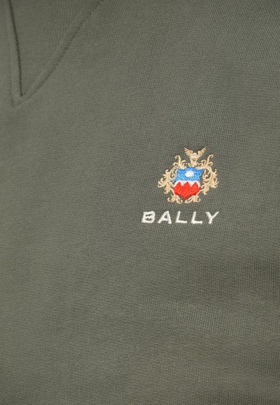 Roheline kangas, millel on tikitud Bally logo, mis sisaldab sinist ja punast kilpi, kullaga dekoratiivne joonistus üleval ja valge tekst all.