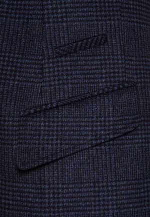 Granatowa marynarka w kratkę z teksturowanej mieszanki wełny. Posiada wywijany kołnierz oraz dwie skośne kieszenie. Subtelne detale w wzór jodełki.