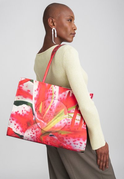 Tasche mit einem lebhaften rosa Blumenmuster, aus Stoff mit stabilen roten Griffen. Kreisförmige Details auf der Vorderseite verleihen Dimension.