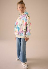 Kapturowa bluza z wielokolorowym nadrukiem graffiti, luźny krój, zestawiona z szerokimi jasnoniebieskimi dżinsami i białymi trampkami.