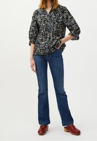 Blusa nera con motivo floreale e bottoni blu a contrasto, abbinata a jeans blu a zampa d'elefante e zoccoli rossi, caratterizzata da una vestibilità comoda e maniche a tre quarti.