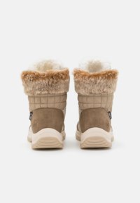 Bottes imperméables marron avec des poignets en fourrure, des côtés matelassés et des semelles en caoutchouc. Présente des accents beiges et une étiquette de logo au talon.