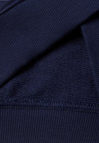 Tejido azul marino que presenta una superficie acanalada suave y una textura de toalla debajo, con costuras visibles en el borde.