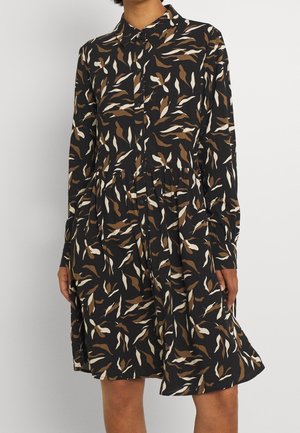 Zwarte jurk met lange mouwen en een bruin-wit abstract bladpatroon, met knopen aan de voorkant en een gerimpelde taille, gedragen door een staande persoon.